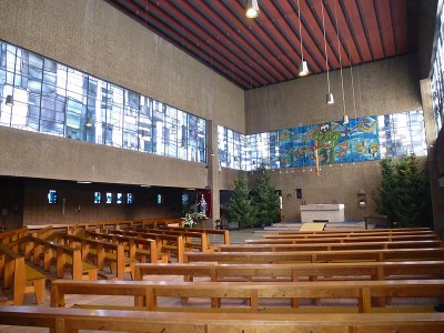 Foto: Dieter Wintz[/caption]

Die Kirche St. Rochus Jülich ist vom berühmten Architekten und Bildhauer Prof. Gottfried Böhm geschaffen worden, emeritierter Professor für Werklehre (später Stadtbereichsplanung und Werklehre) an der RWTH Aachen. Etwa 70 Sakralgebäude in Deutschland tragen die Handschrift Böhms, darunter im Bistum Aachen die St. Hubertus Kirche, Aachen- Hanbruch, und St. Rochus, Jülich.

Dabei hat Böhm für seine charakteristisch skulpturenhaften Bauwerke vor allem die Bauston, Stahl und Glas verwandt. Auch die Rochuskirche ist von Böhms aufs Wesentliche reduziertem Stil geprägt: klare, kubische Form ohne Schnörkel und anderen Zierrat.

Das Altarmosaik hat der Eupener Künstler Peter Paul Jacob Hodiamont geschaffen, die Kirchenfenster sind durch Hubert Spierling gestaltet worden (Detailansichten der Kirchenfenster finden Sie auch auf den <a href=